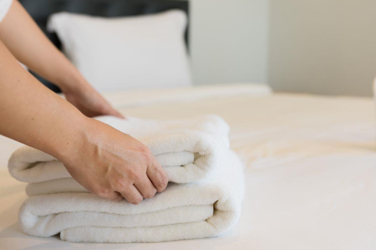 Housekeeper folding fresh towels on a bed