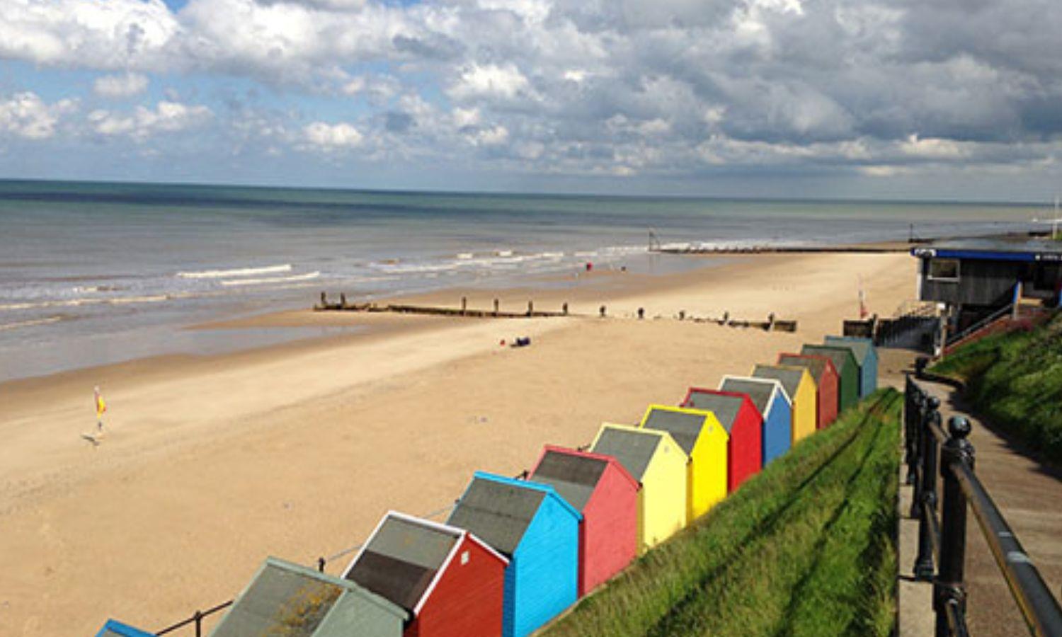 Colourful beach huts lining sandy Mundesley Beach