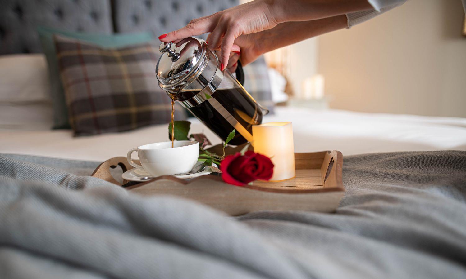 Woman pouring coffee into a cup on a tray with a lit candle and red rose