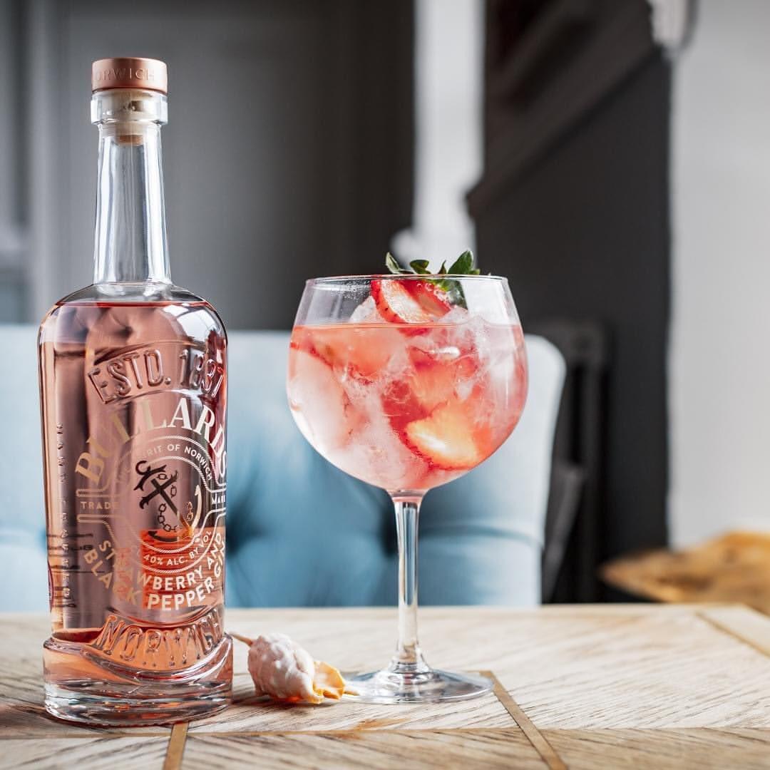 Pink gin bottle with G&T in glass with strawberries
