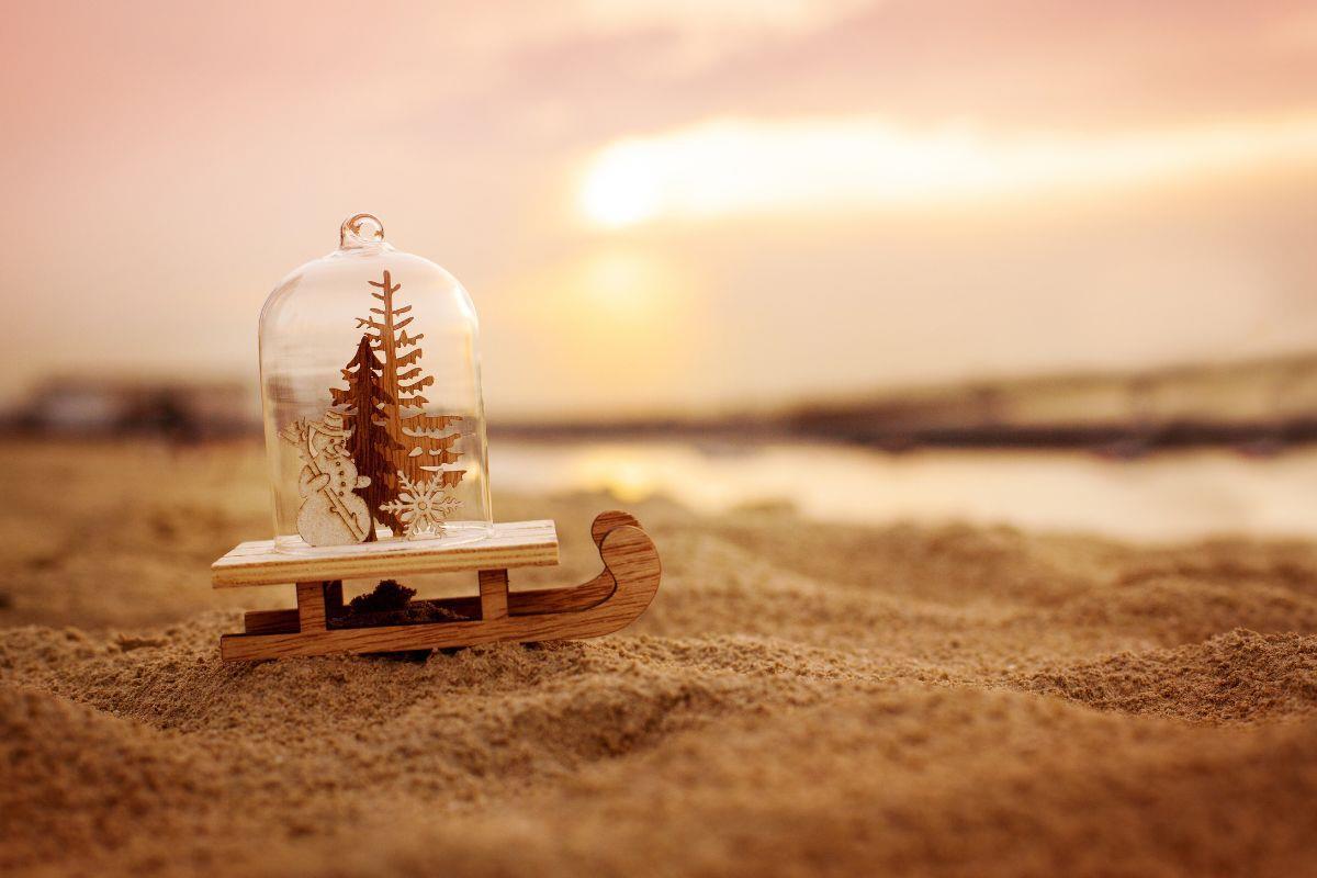 A christmas tree snowglobe, sat on the beach at sunset.