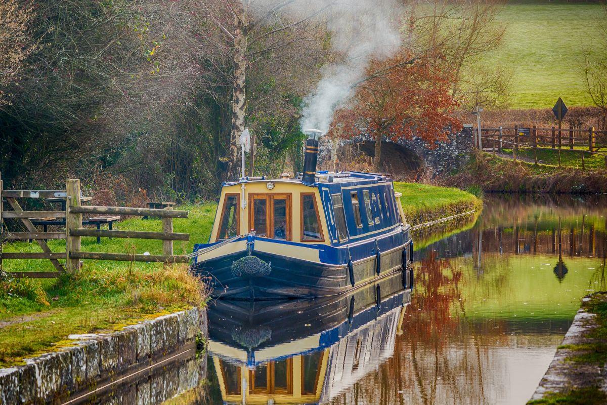 Autumn scene of canal boat moored up with smoke rising from the chimney. Photo credit: Adobe Stock
