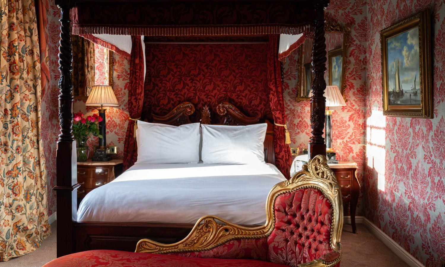 Ornate four poster bed in a richly designed bedroom with red patterned wallpaper
