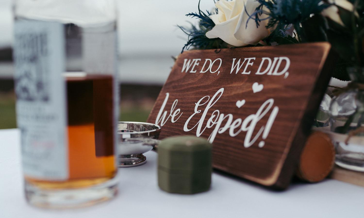 Sign saying we do, we did, we eloped on table surrounded by flowers