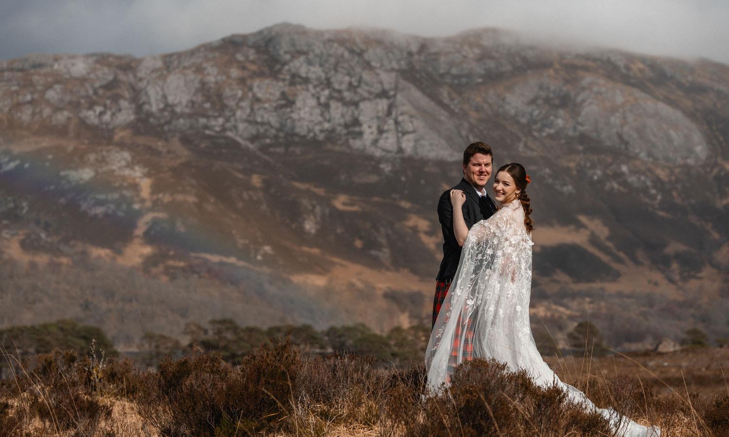 Wedded couple embracing on highland heath with mountains in the background