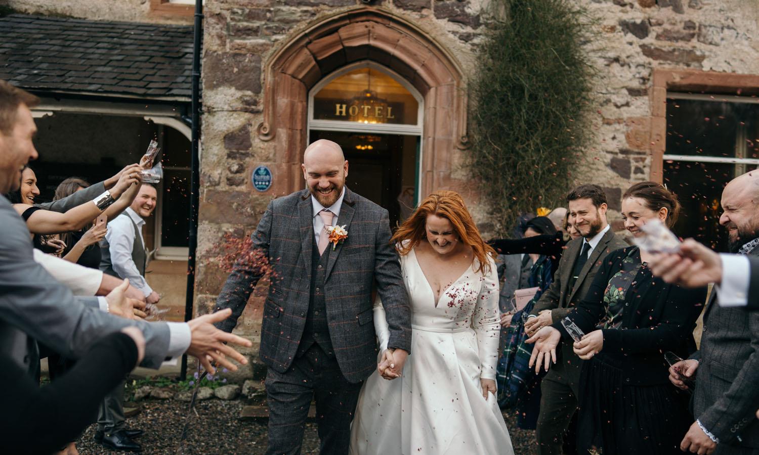 Couple leaving hotel with guests showering them with confetti