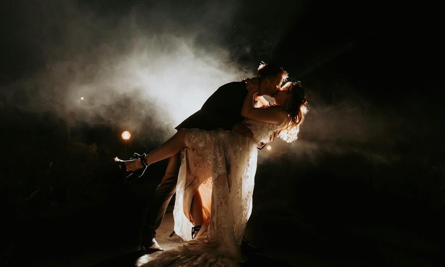 Bride and groom embracing outside lit by fireworks 