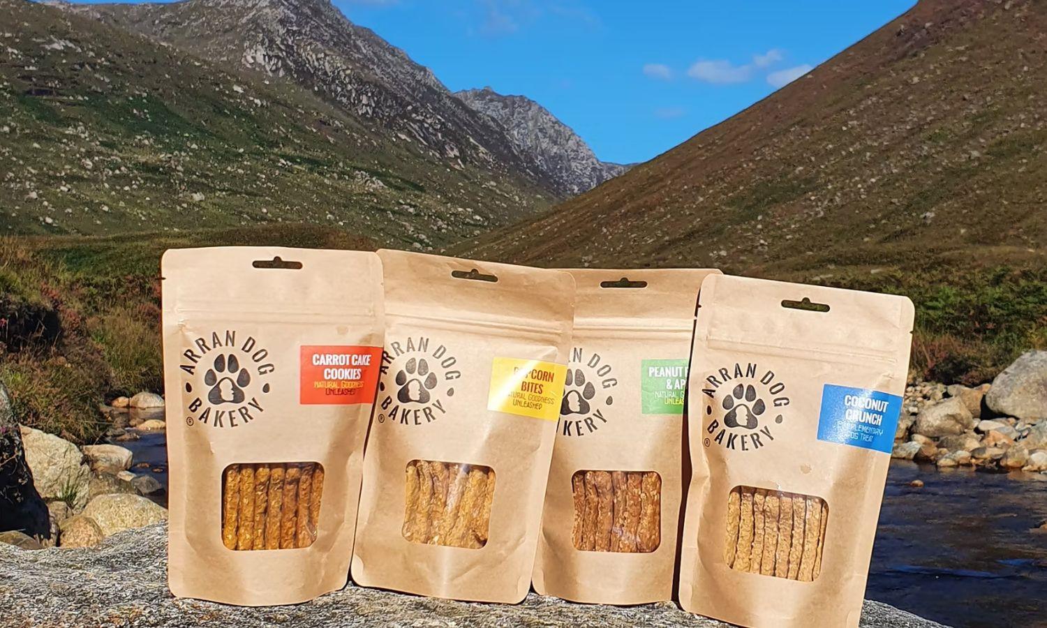 Four bags of dog treats lined up on rocks in mountainous landscape
