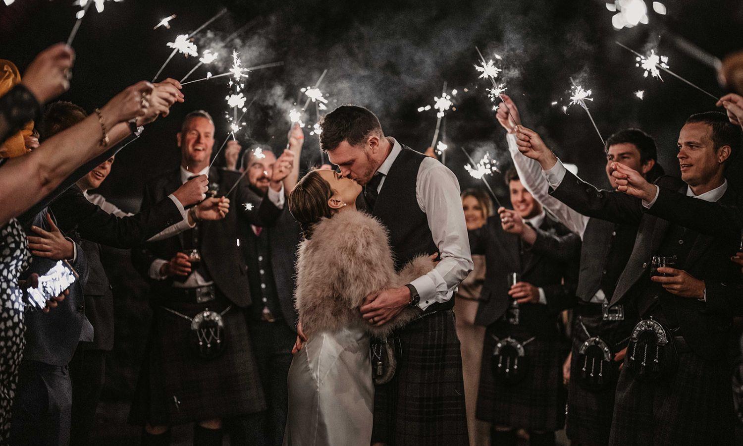 Bride and groom kissing with friends and sparklers on a winter night