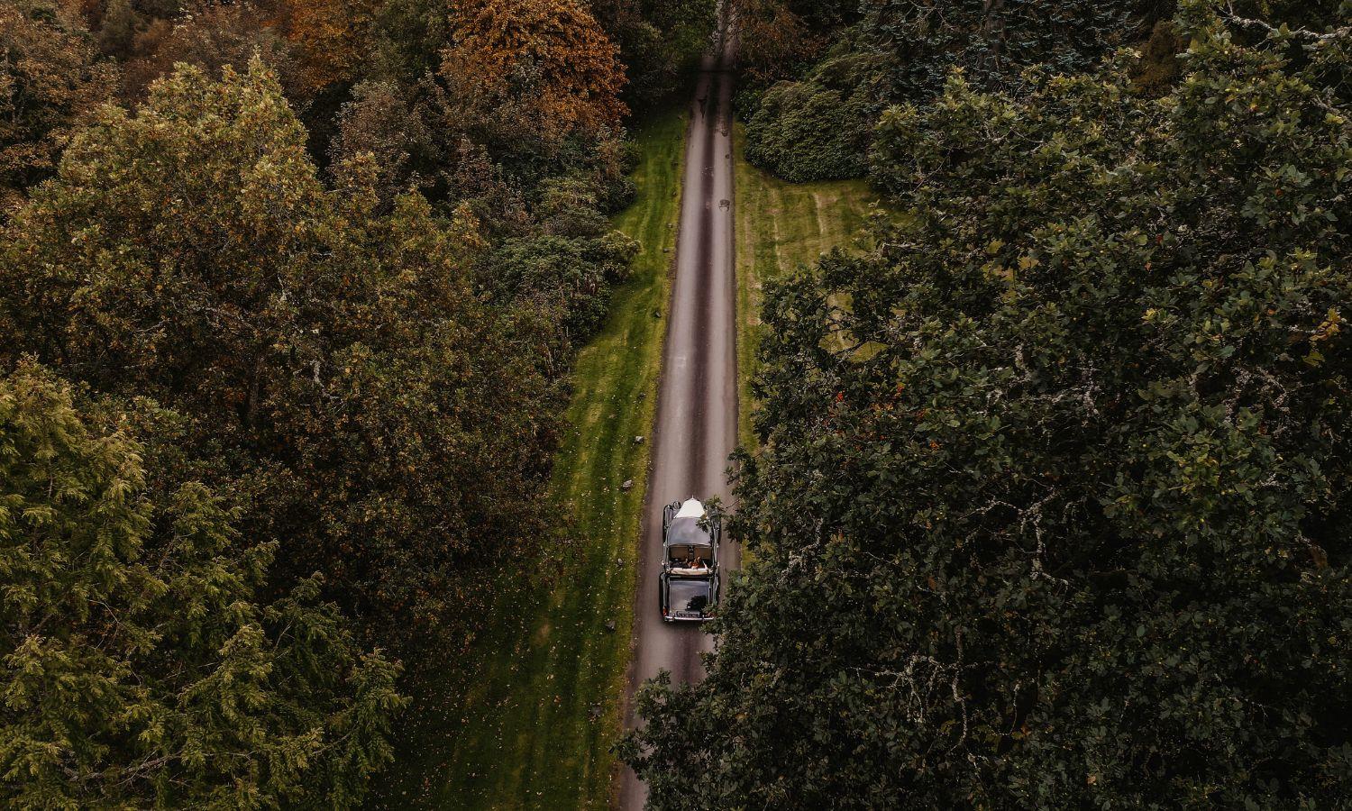 Classic wedding car arriving along the tree-lined driveway at Auchen Castle