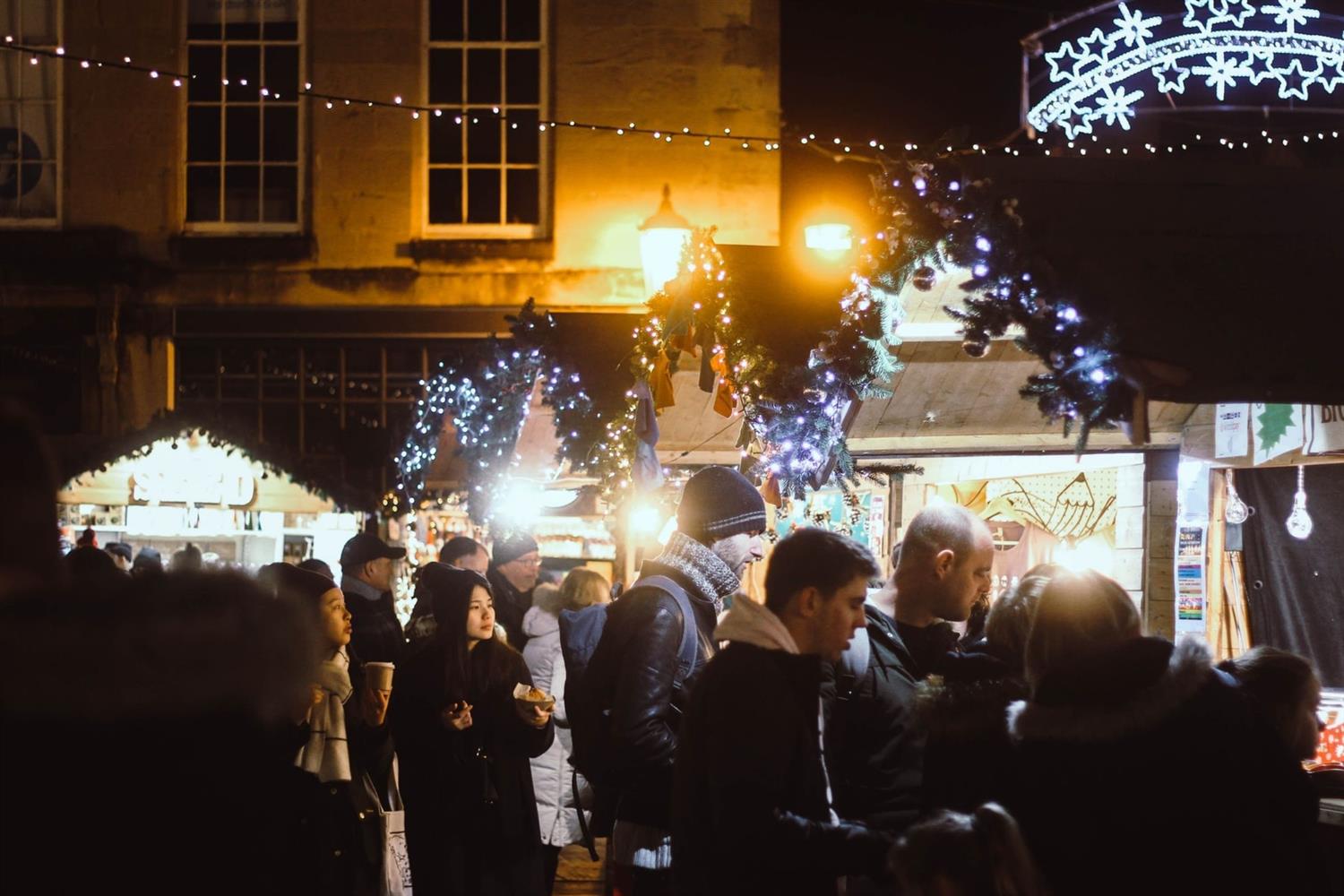 People shopping at outdoors stalls in the evening at Bath Christmas Market