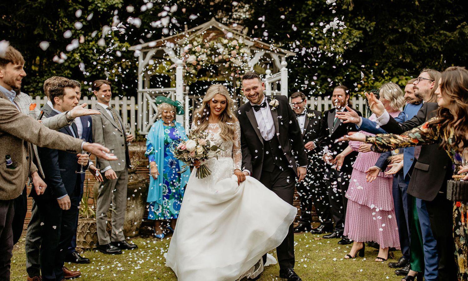 Newlywed couple at outdoor wedding ceremony with confetti being thrown