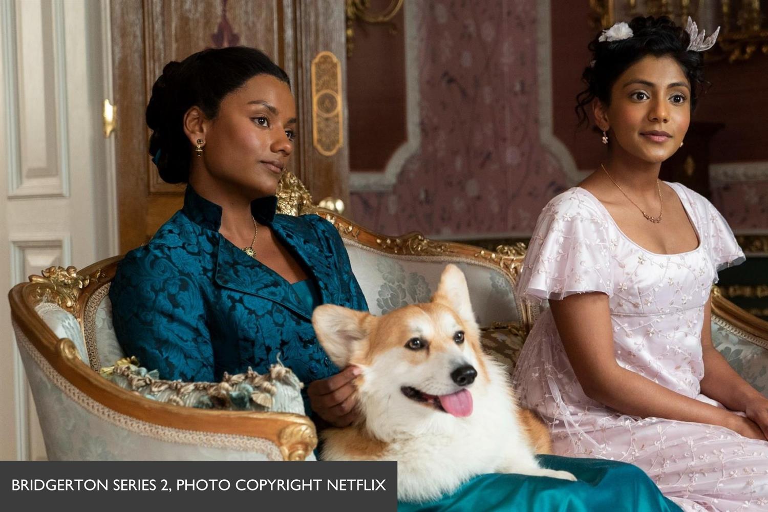 2 Bridgerton actresses sitting on sofa with corgi