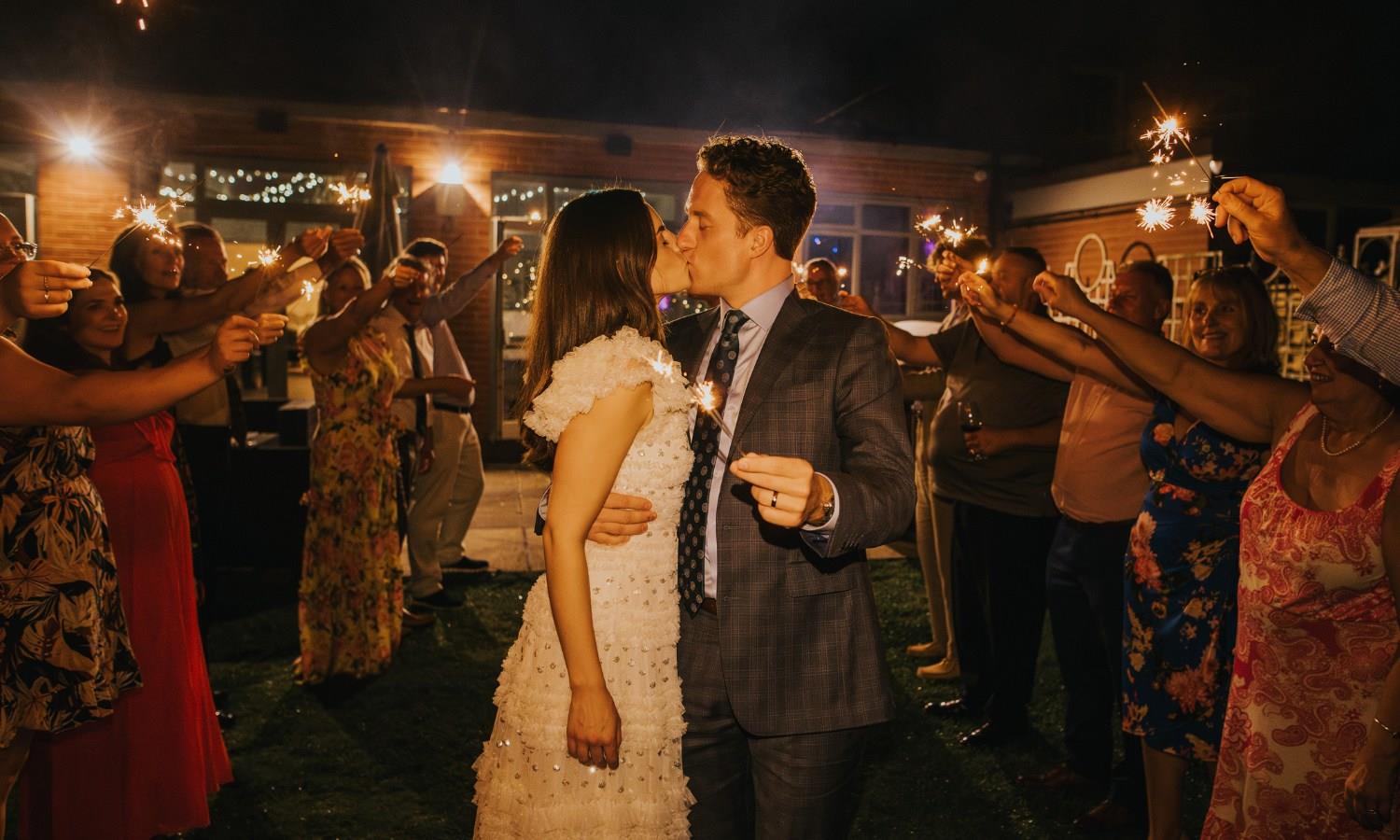 Newlywed bride and groom kissing surrounded by guests holding sparklers