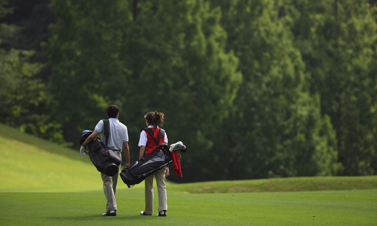 Lady and man walking on golf course carrying golf club bags