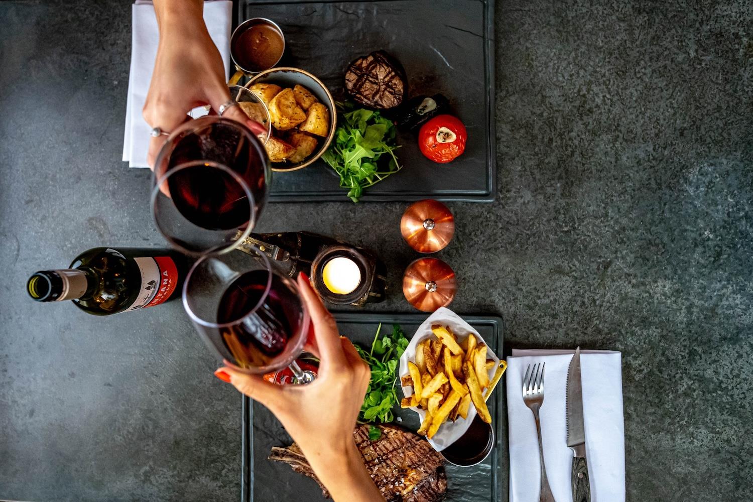 Toasting two glasses of red wine over steak and chips