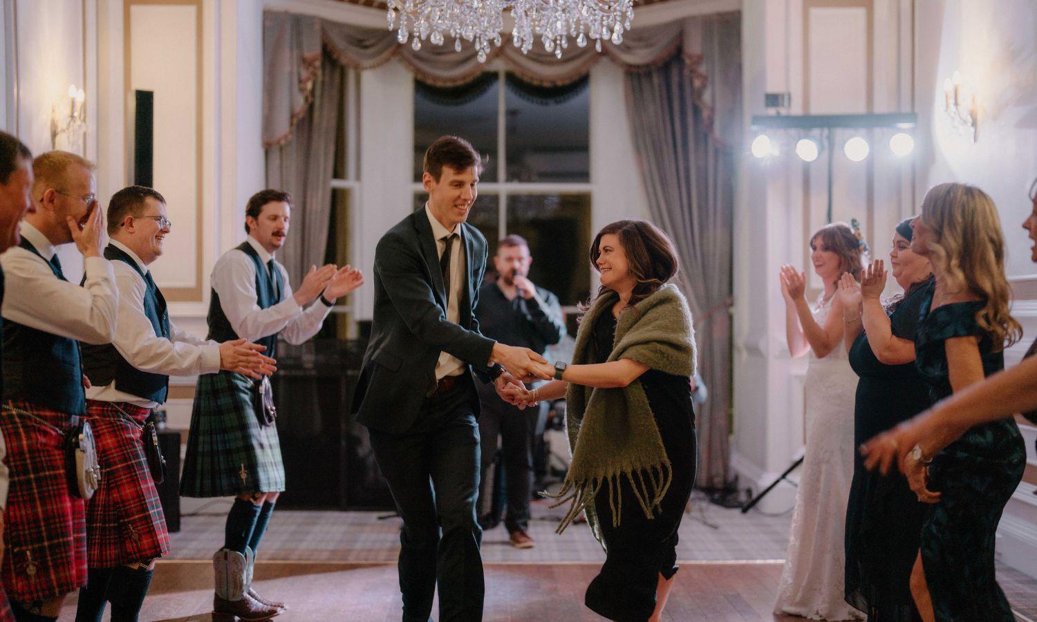 Ceilidh dancing at wedding reception with guests in kilts celebrating in the historic ballroom