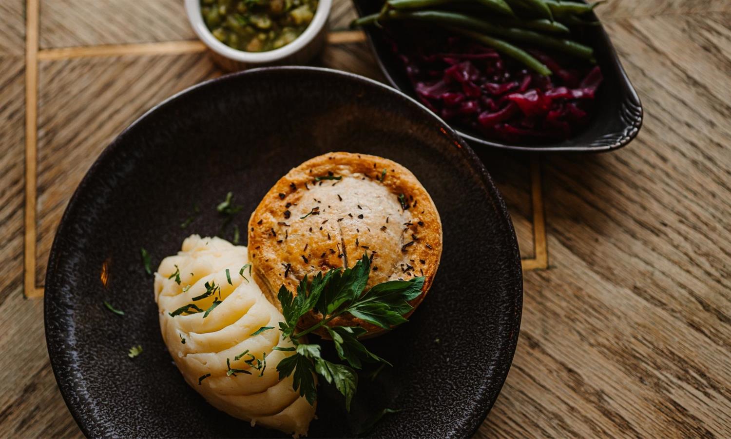 Pie with mash and separate vegetables on a wooden table at The Ship Inn