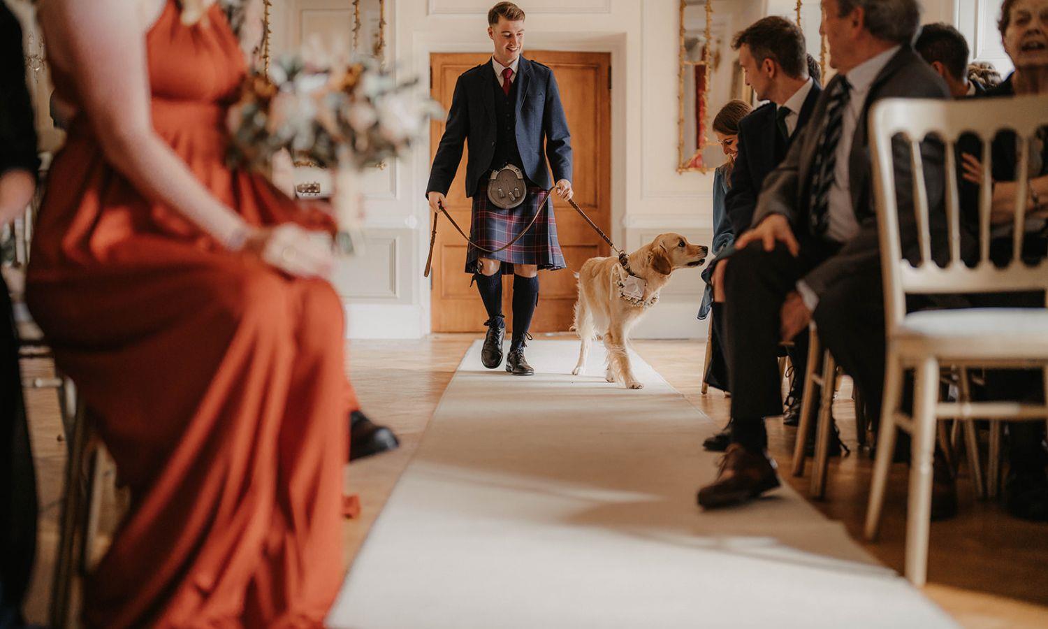 Bestman walking down the aisle with family dog at a Scottish castle wedding ceremony