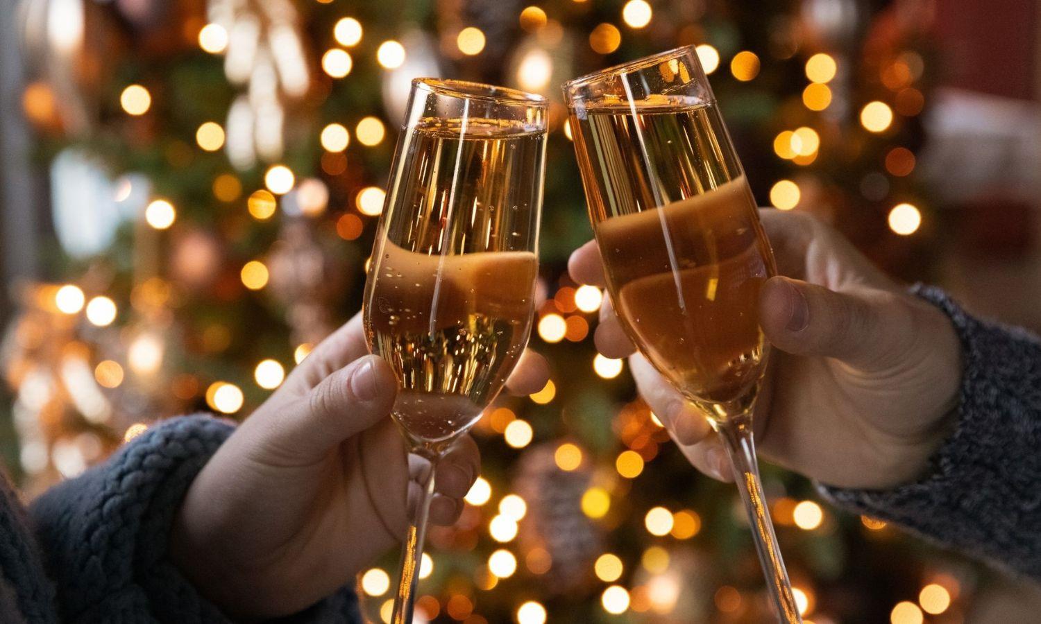 Two people raising a glass of fizz in front of Christmas tree lights