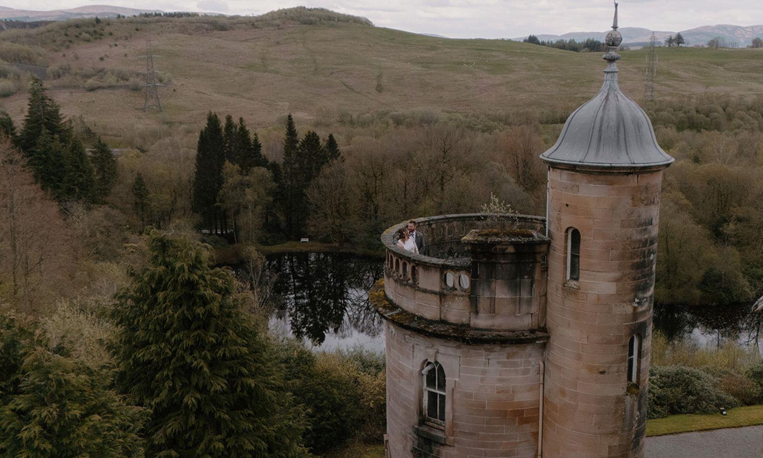 Bride and groom on the turret balcony at Auchen Castle overlooking Scottish countryside