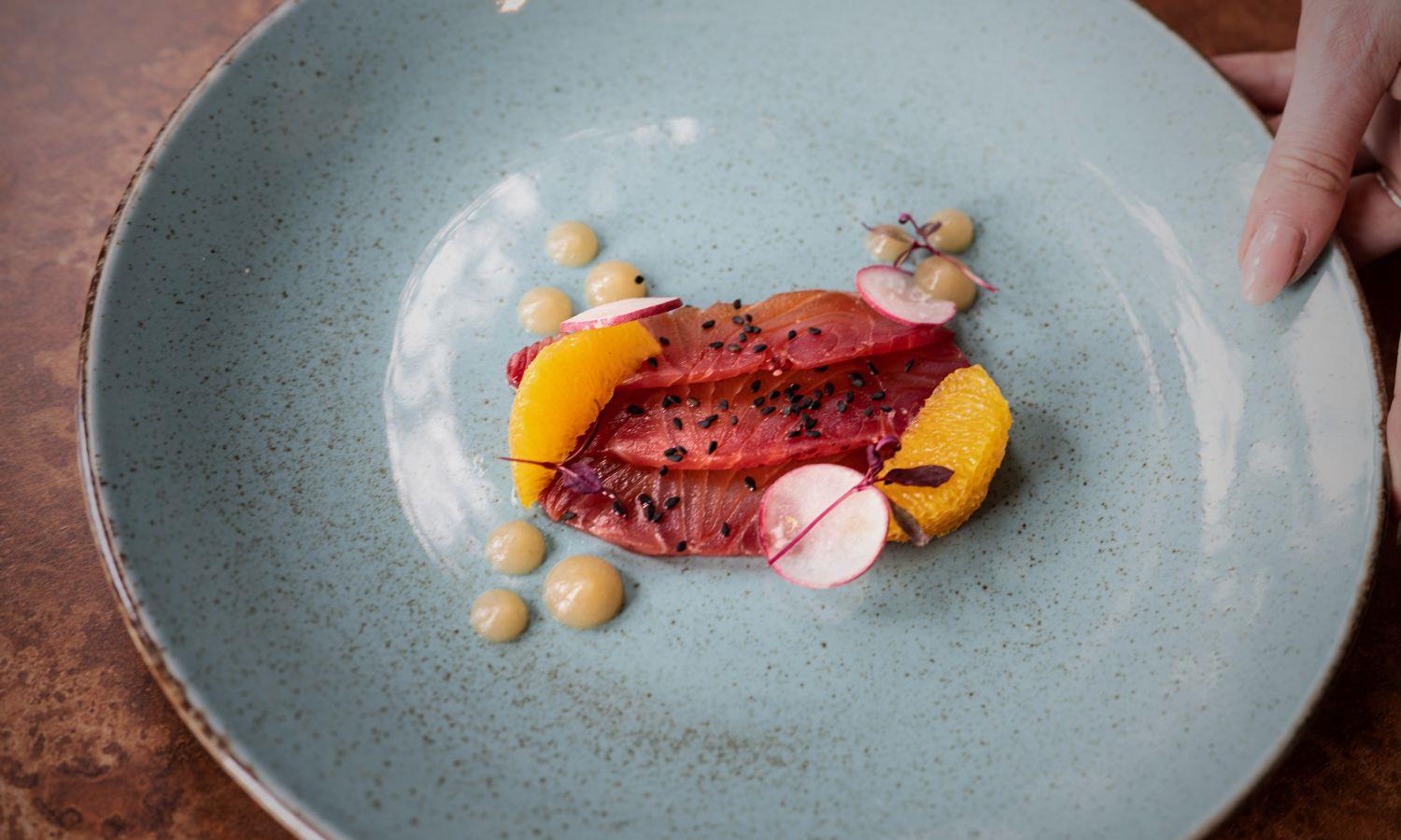 Waitress placing plate with fine dining style pickled salmon