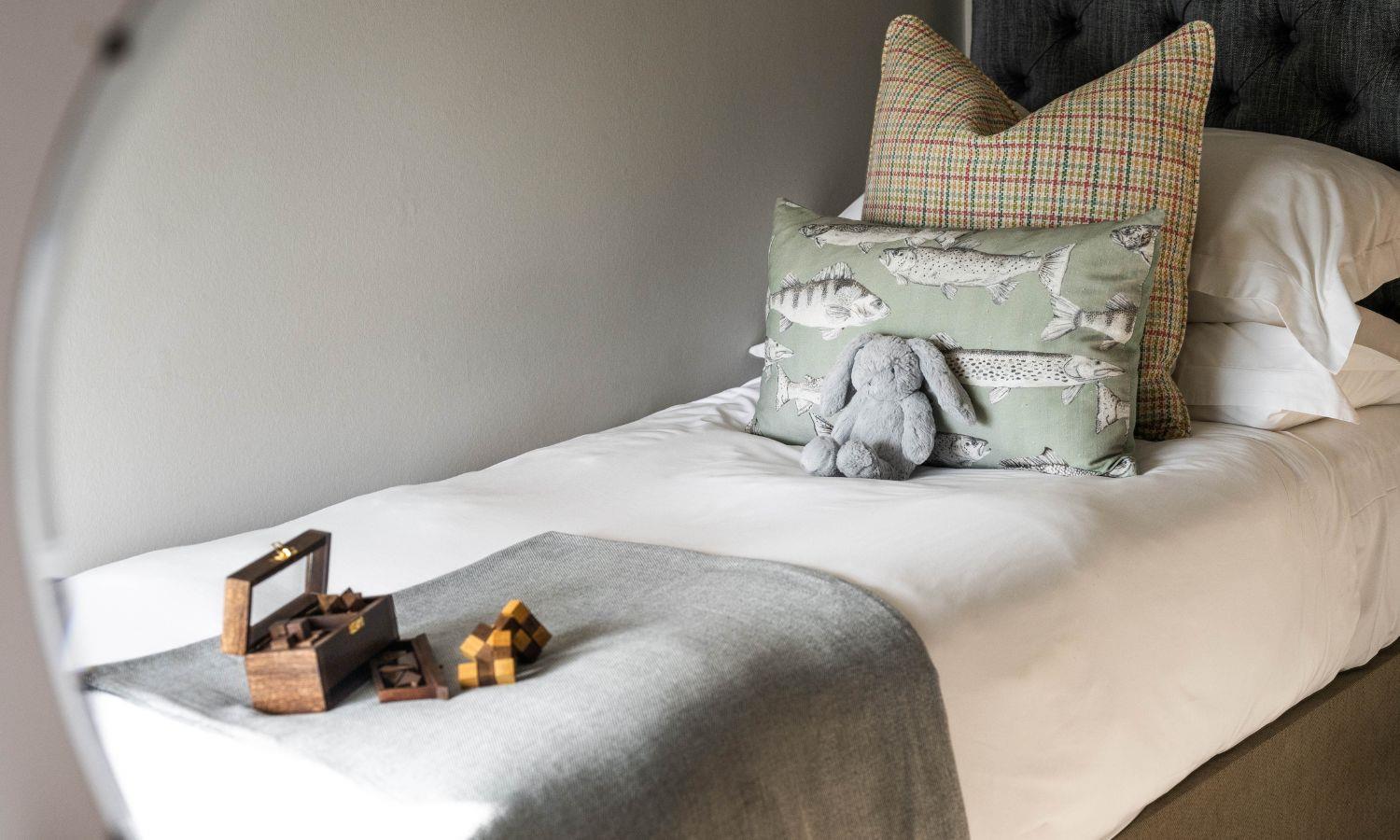 Single bed with cushions, bunny cuddly toy, and game, in hotel family bedroom