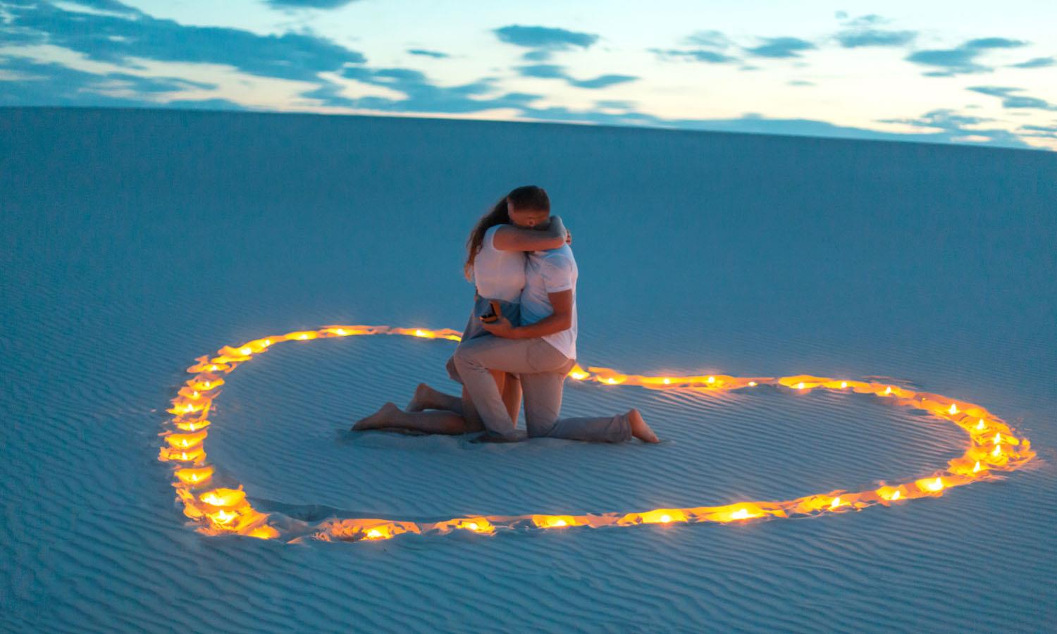 Woman hugging man inside heart of candles on a moonlit beach