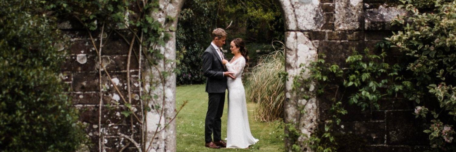 Bride and groom standing under a flower covered stone archway