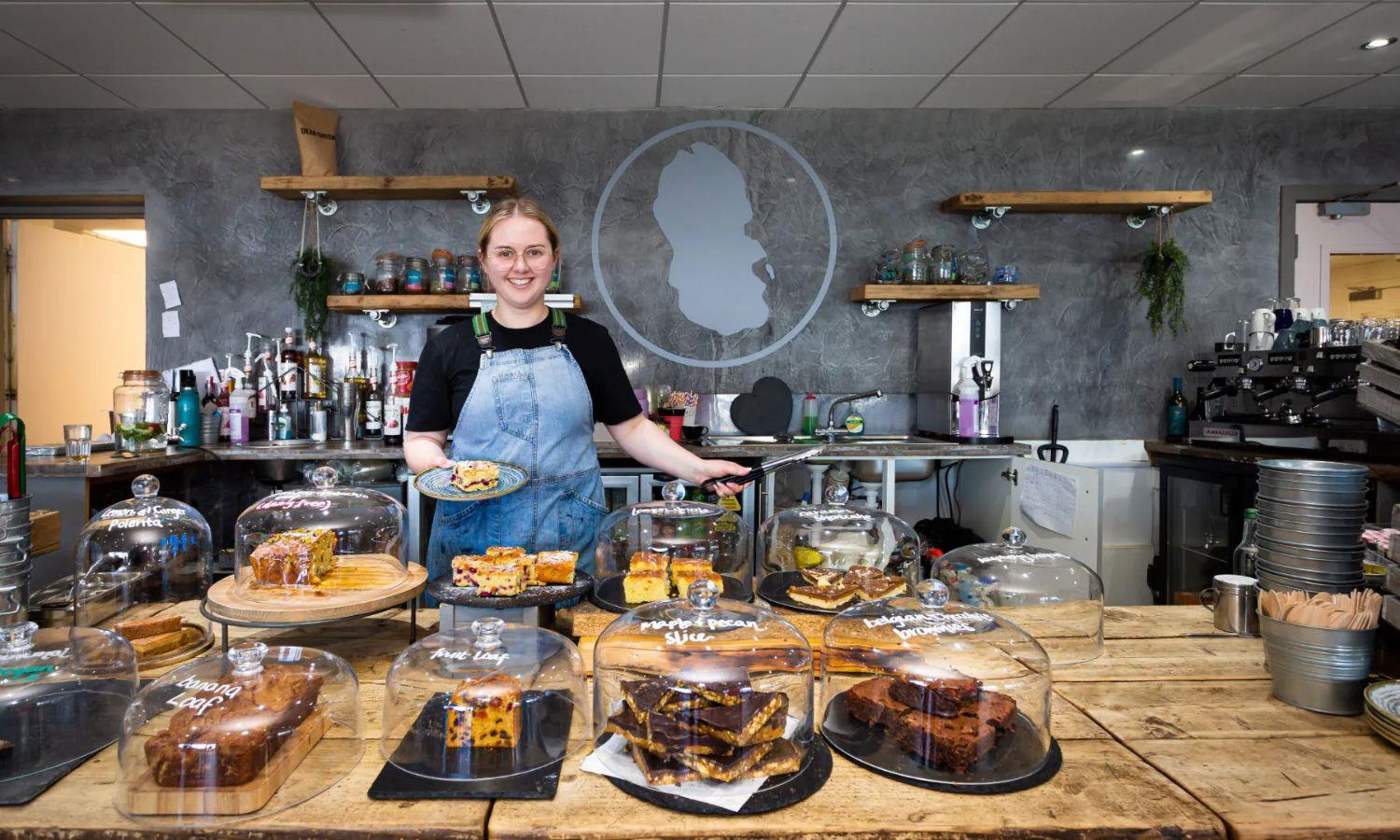 Lady working in cafe with selection of cakes on display
