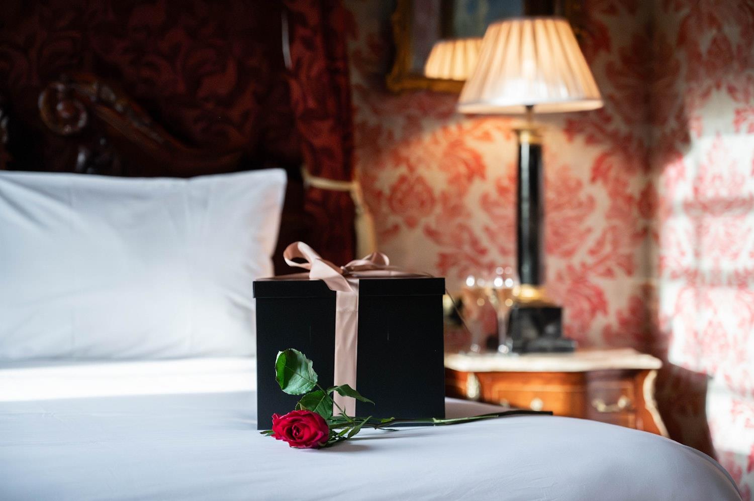 Gift wrapped box and red rose lying on a bed