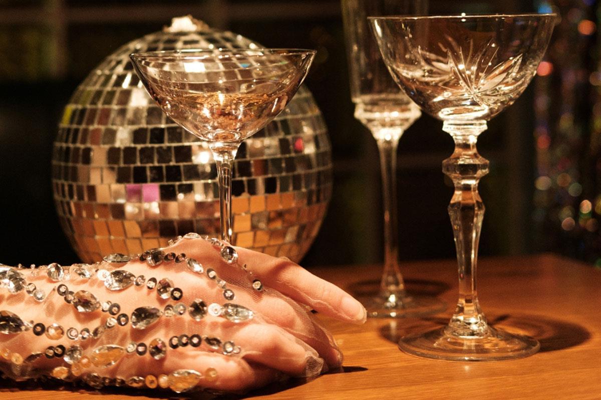 Woman's hand covered in jewels holding a glass on a table with a disco ball