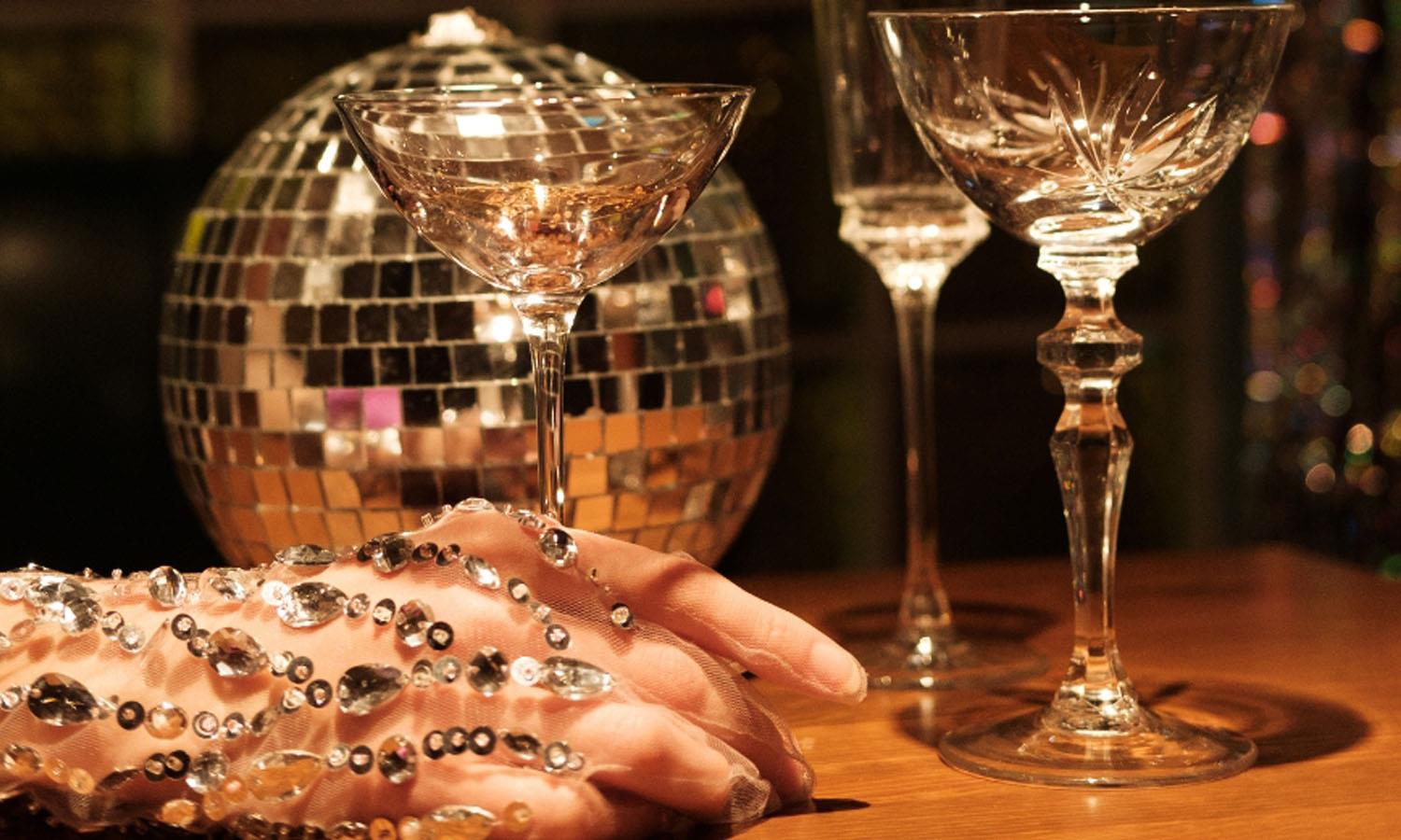 Woman's hand covered in jewels holding a glass on a table with a disco ball