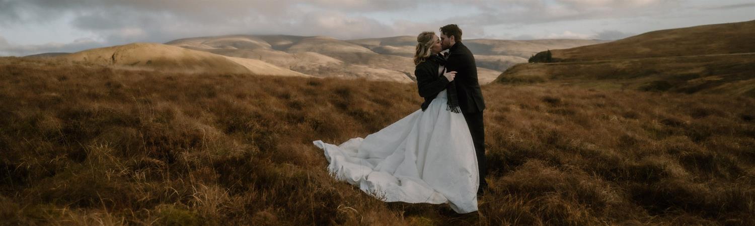 Bride and groom kissing against a backdrop of wild hills in Scotland