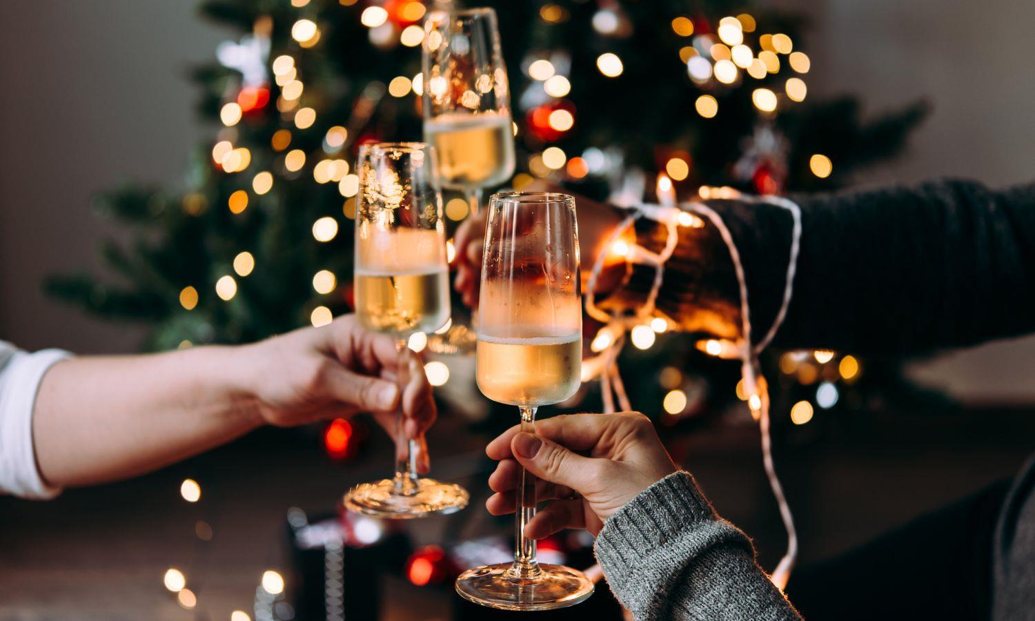 Hands clinking glasses of Champagne in front of a Christmas tree