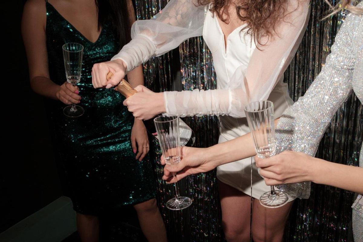 Girls in sparkly dresses popping champagne