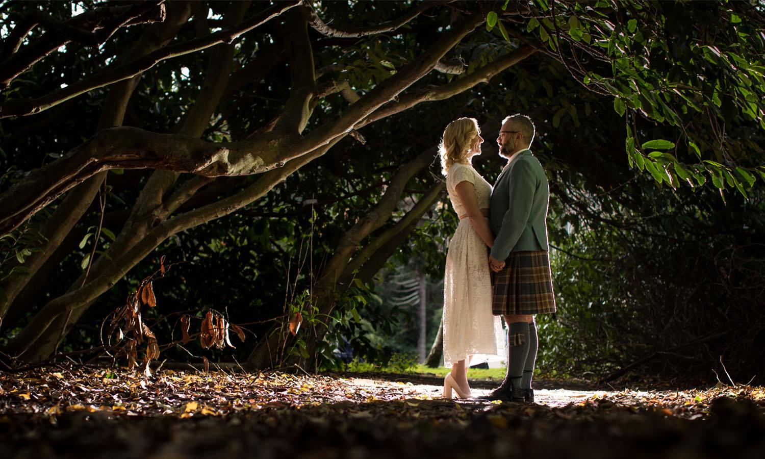 woman in wedding dress and man in kilt in a wood