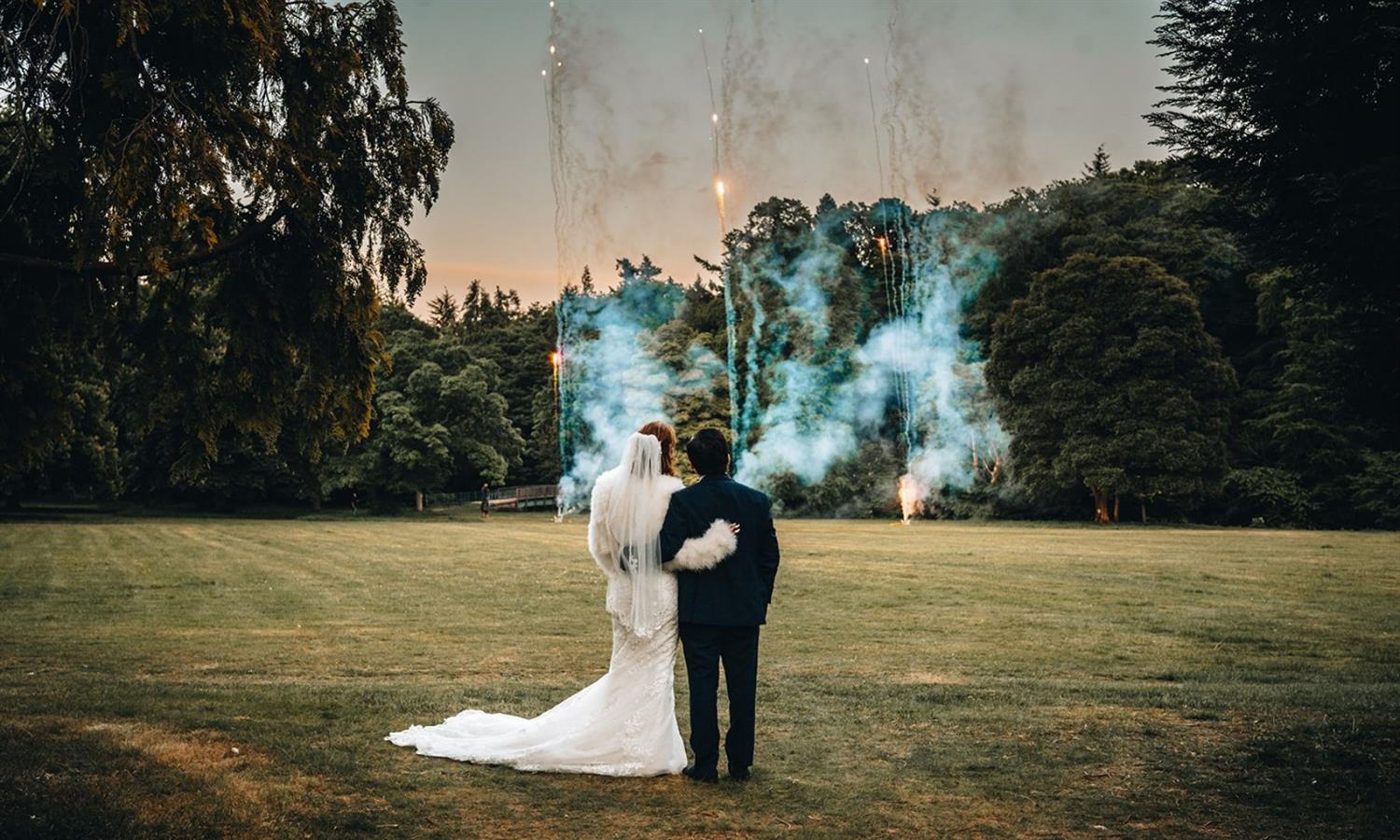 Bride and groom watching fireworks in beautifully manicured grounds