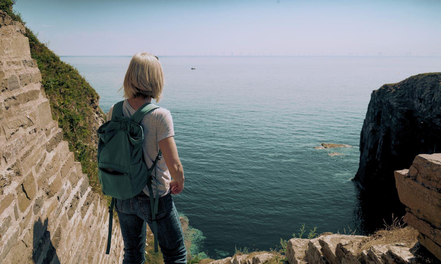 Hiking lady looking at the sea from the entrance of Whalingoe Harbour in Caithness on a sunny day