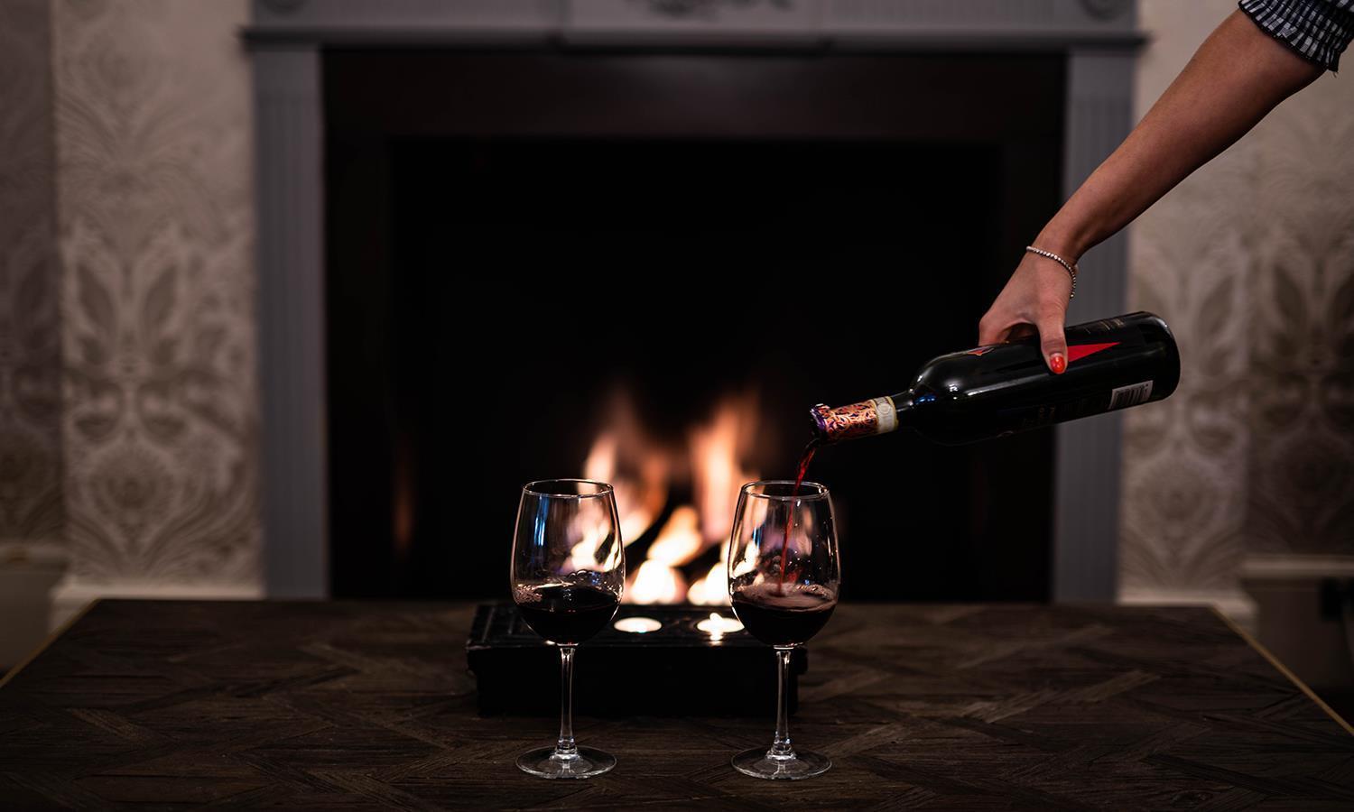 Wine being poured into a glass in front of a roaring fire