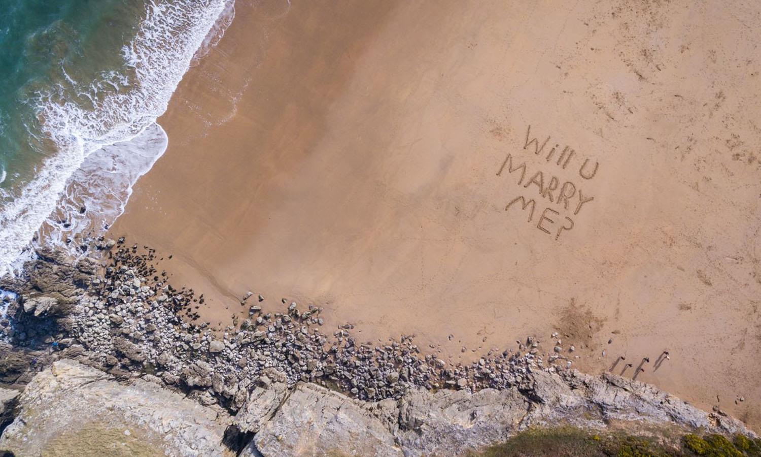 Will you marry me written in sand seen from top of cliff