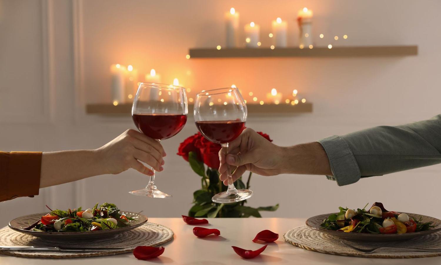 2 people clinking glasses of wine at dinner with red roses