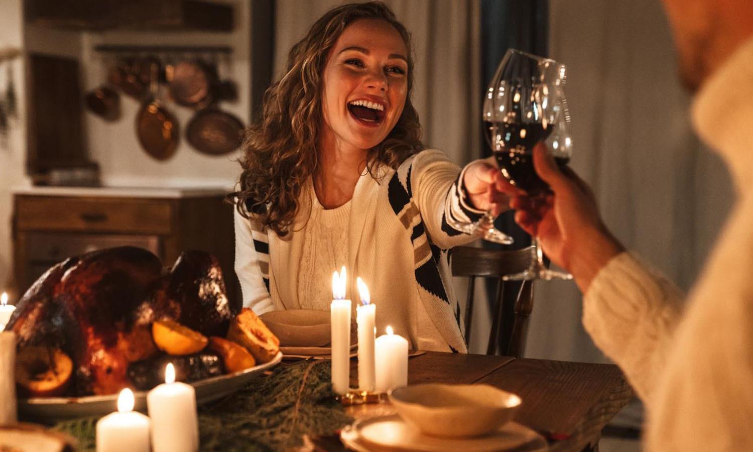 Woman clinking glasses with man over dining table with candles