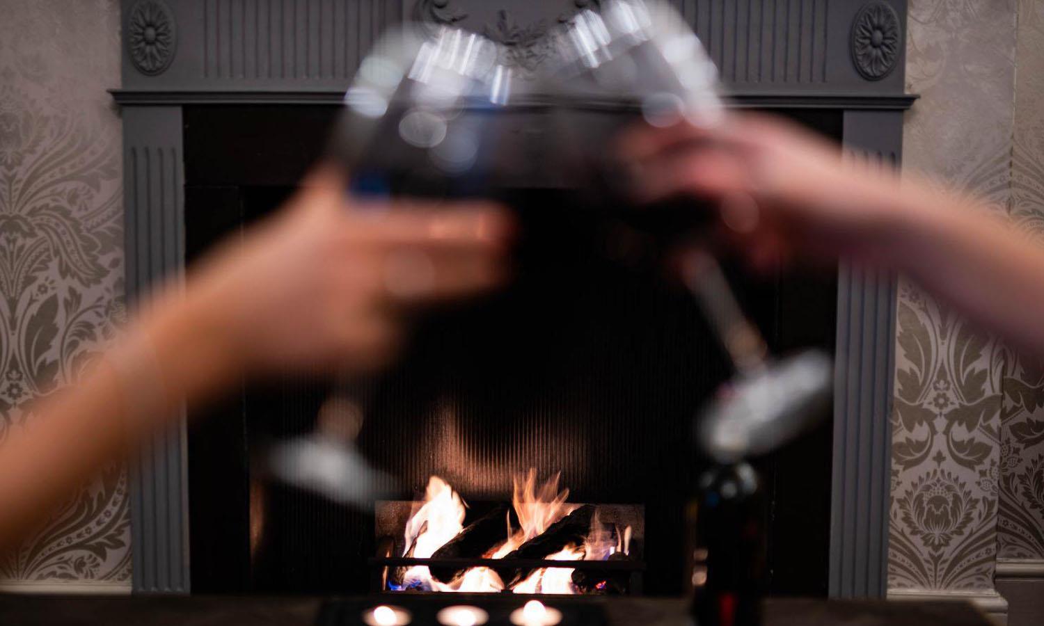 Two glasses being clinked together in front of open fire