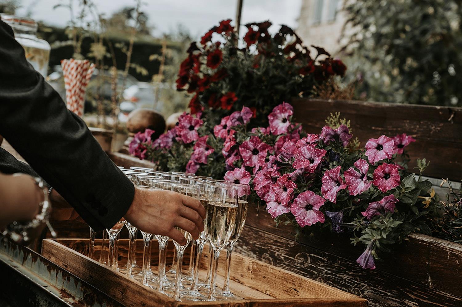 Guest takes a glass of fizz off a tray with flowers in the background (c) Amber Louise Photography