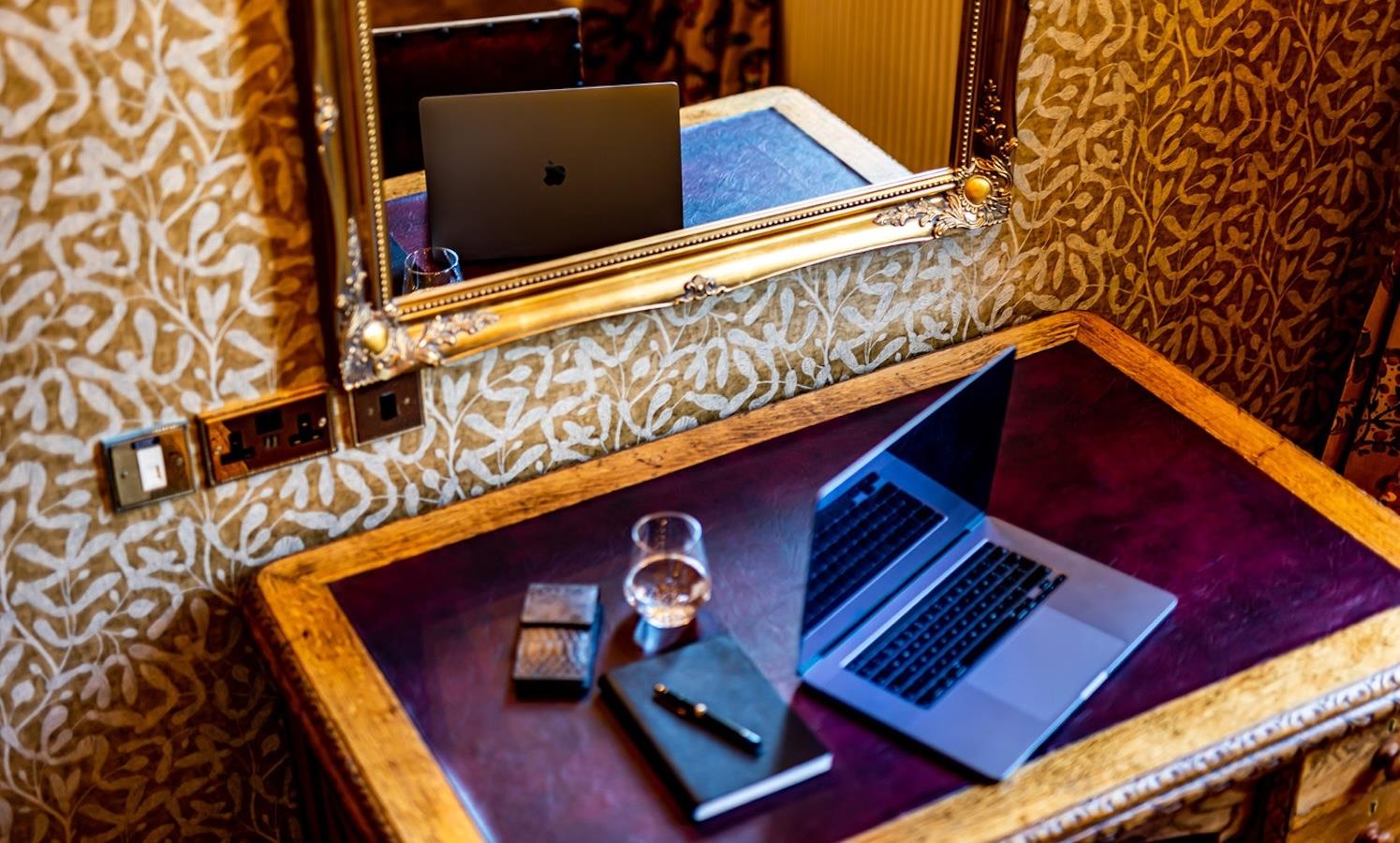 A laptop set up on a vintage desk with patterned wallpaper
