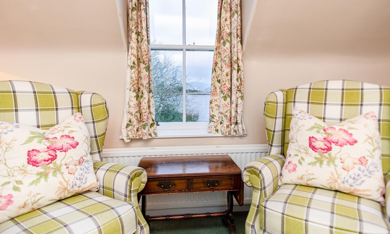 2 decorated chairs either side of small table and window with floral curtains