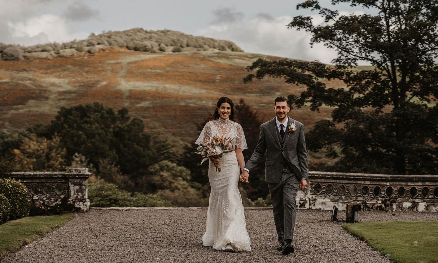 Newlyweds walking hand in hand in grounds of a castle with Scottish countryside