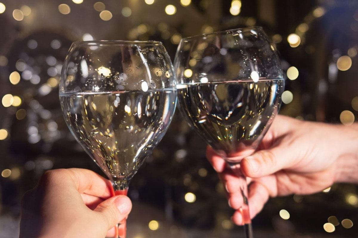 Two  wine glasses being clinked together in front of festive lights