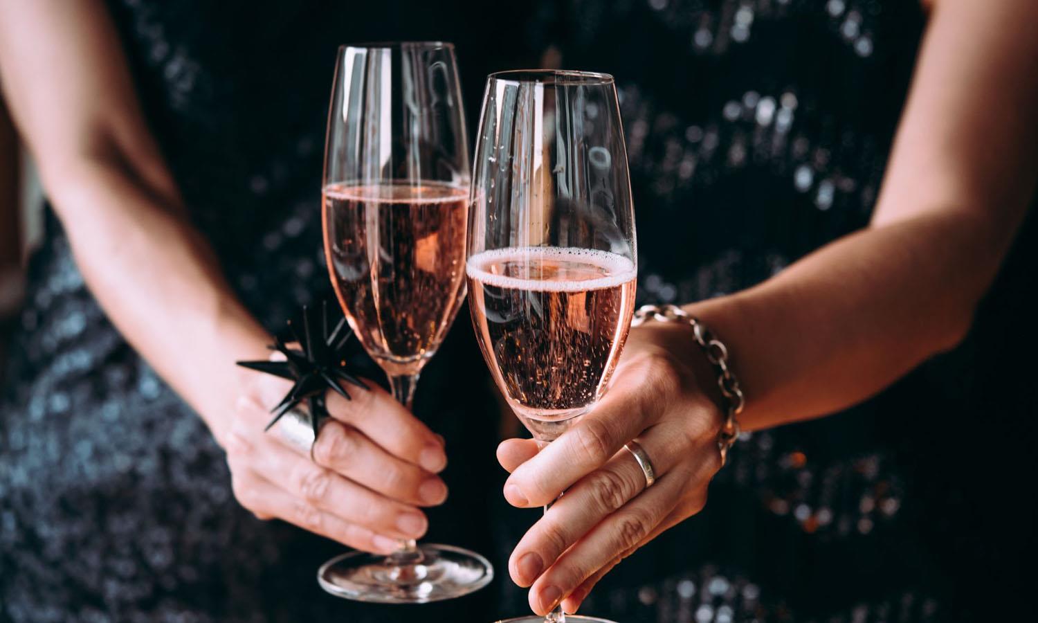 Woman in party dress holding two glasses of pink fizz in Champagne flutes